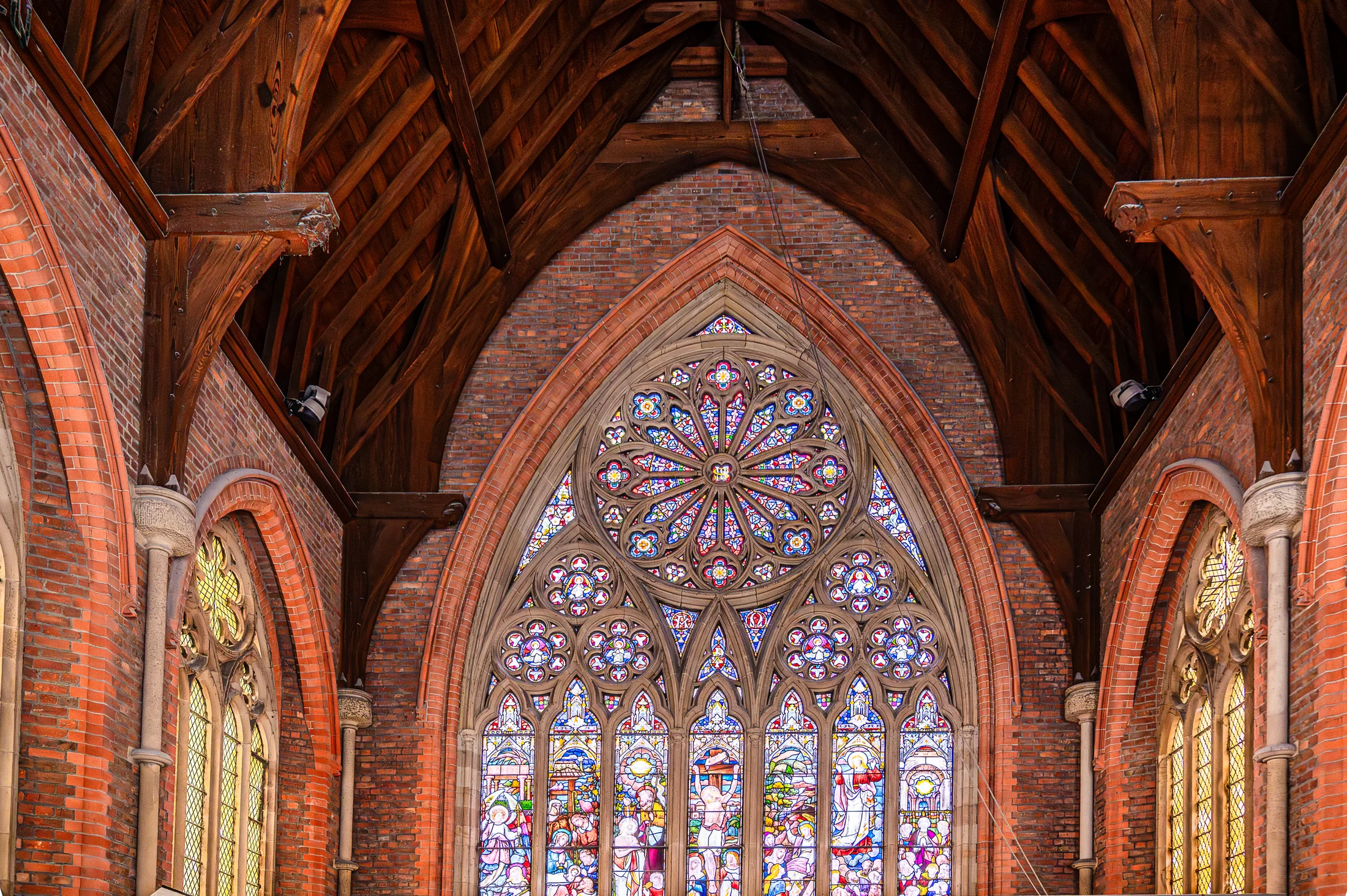 A large stained-glass window framed by brick arches beneath the timber roof